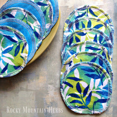 Reusable pads with blue, green, and white floral pattern, white stitched edges, and "Rocky Mountain Herbs" text visible