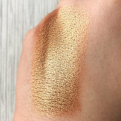 Close-up of a fingertip applying copper eye shadow pigment with shimmering metallic finish to eyelid