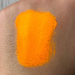 Close-up of vibrant neon orange eye shadow pigment with intense color payoff in a small 2ml container