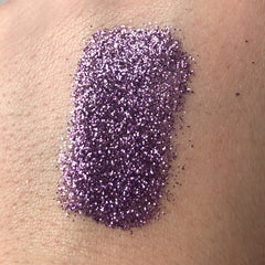 Purple glitter makeup swatch on skin, showing fine particles and texture