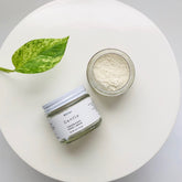 Facial Cleanser in glass jar with white lid, beige powder, and green leaf on white surface