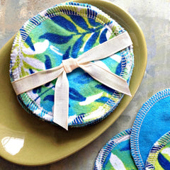 Reusable facial rounds with blue and green floral pattern, white stitched edges, and cream ribbon bow
