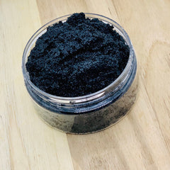 Black glitter in clear plastic jar on light wood surface