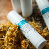 Skin care balm, white tube with blue label, surrounded by dried flowers, Chloemason brand visible