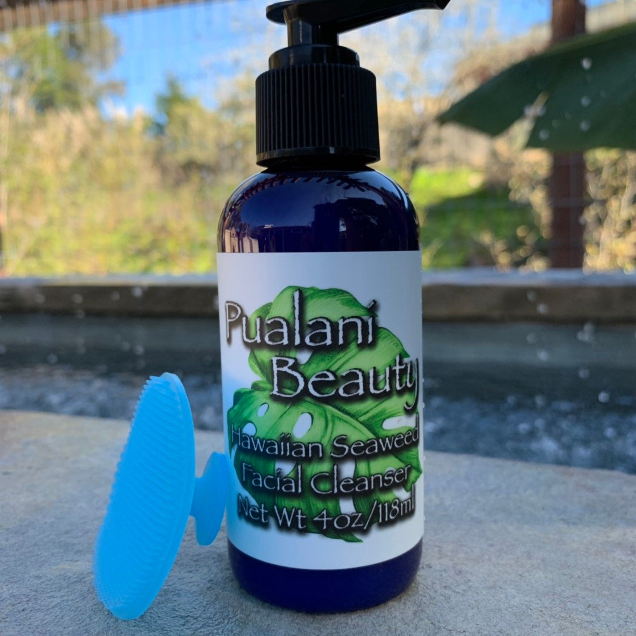 Facial cleanser bottle, dark blue glass, black pump, with blue silicone brush