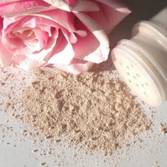 Face powder with beige powder, pink flower, and white container on a white surface