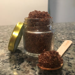 Brown sugar scrub in a clear glass jar with gold lid and wooden spoon, on a marble surface