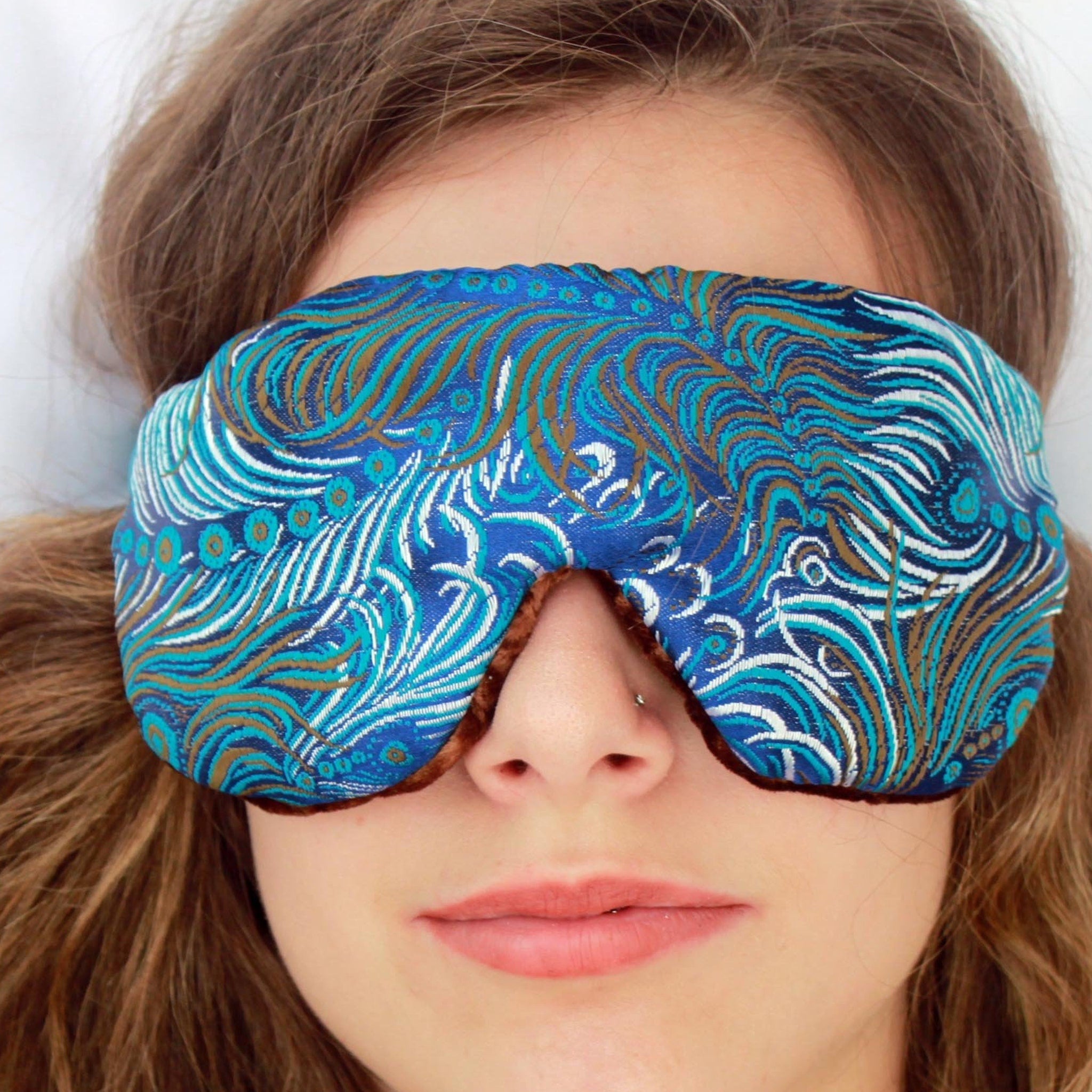 Travel sleep eye mask with blue brocade pattern and brown velvet trim, worn on face