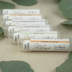 Lip balm tubes with white, orange, and green labels, Wild Jasmine brand visible, on fabric