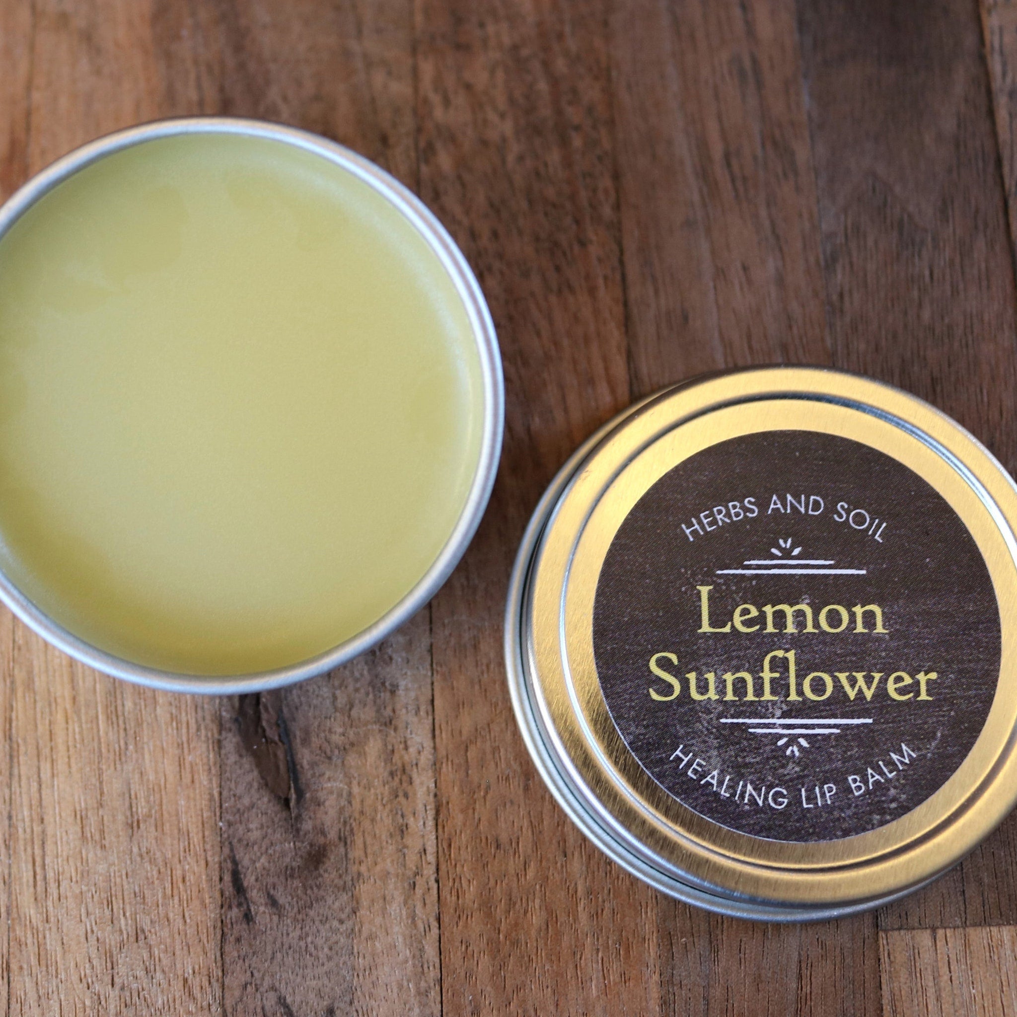 Lip balm in silver tin with yellow balm and Herbs and Soil Apothecary label