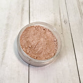Loose mineral foundation in a clear jar with light brown powder on a white wood surface