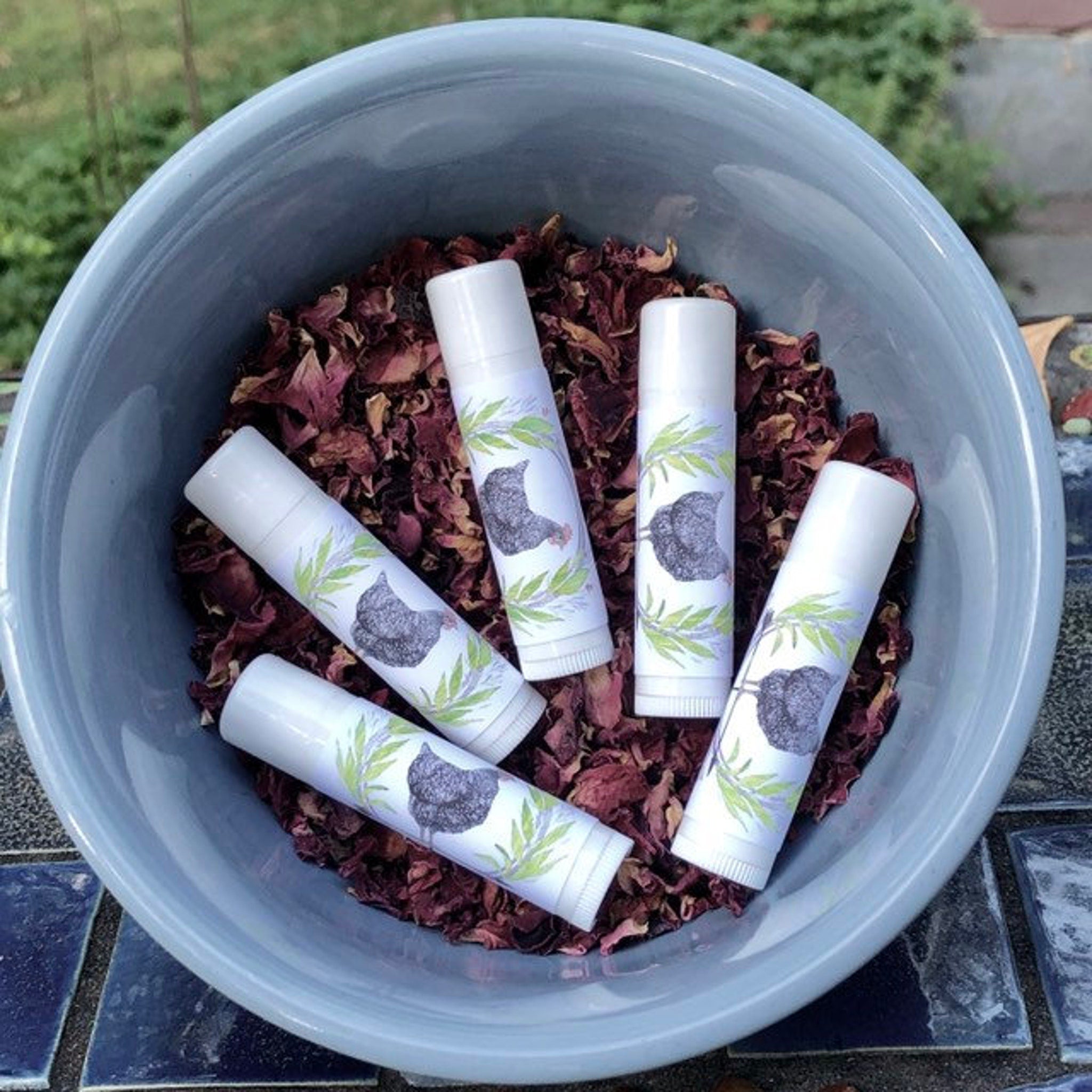 Lip balms white tubes with chicken design in a blue bowl with dried petals