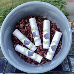 Lip balms white tubes with chicken design in a blue bowl with dried petals