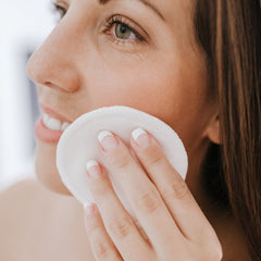 Reusable cotton pad, white circular material, held by hand with french tip nails, used on face