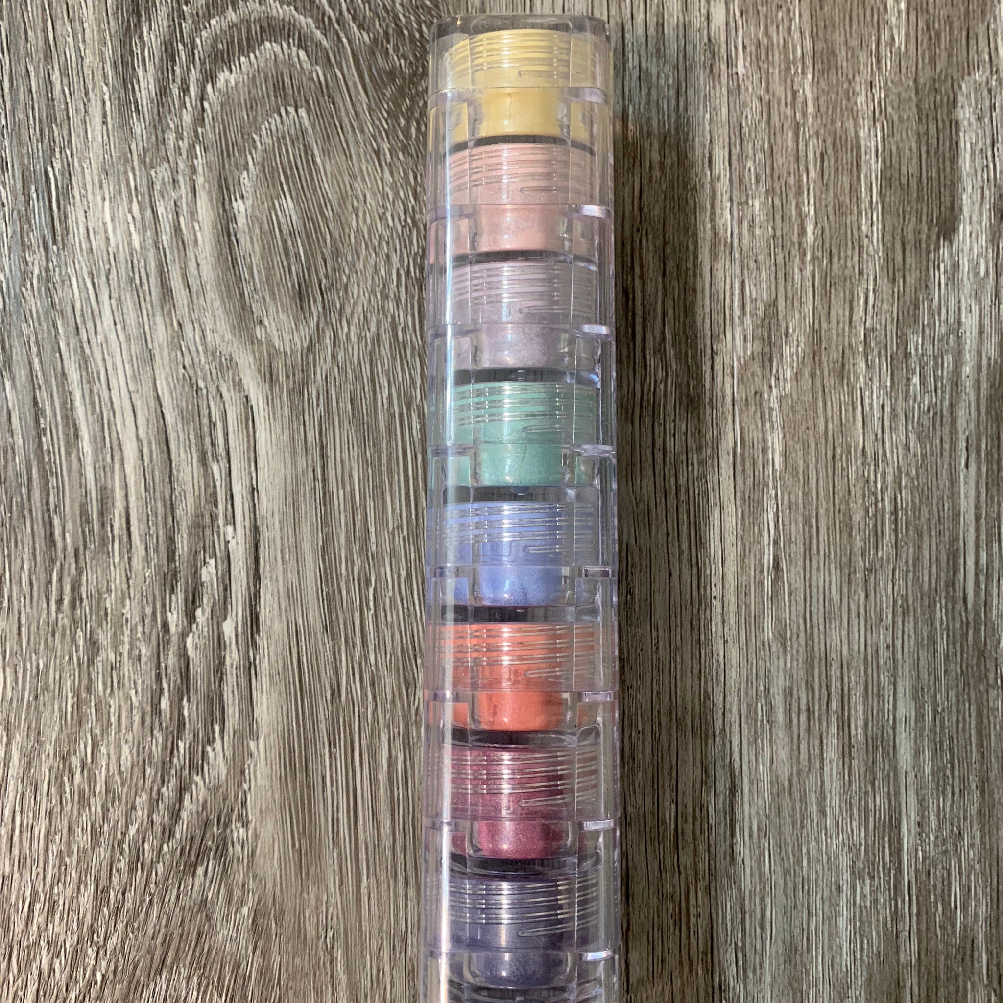 Eye makeup stack with clear plastic case and colorful eyeshadows on wood background