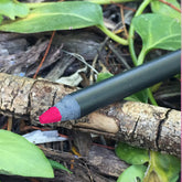 Lip liner pencil, black barrel, pink tip, resting on wood and leaves