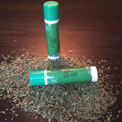 Lip balm tubes, green and white, with "Mint" text, on a bed of herbs