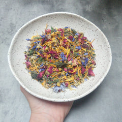 Herbal tea blend with colorful dried flowers in a speckled ceramic bowl held by a hand