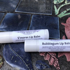 Lip balm tubes, white with printed label, Sanka Family Farm brand, on mosaic tile surface