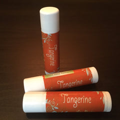 Lip balm with orange and white label, "Tangerine" text, and floral design with Forest Hills Remedies branding