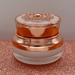 Cosmetic jar with rose gold metallic finish, ornate lid, and clear glass base