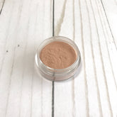 Loose mineral contour in clear jar with light brown powder on white wood background