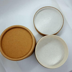 Hand scooping rich cream from a kraft jar onto fingertips for skincare application