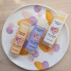 Lip balm tubes in orange, lavender, and white with LB Love branding on a decorated plate