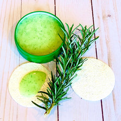 Spirulina face scrub, green jar and scrub with green specks, with rosemary sprig and loofah pad