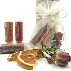 Lip balm tubes with orange, red, and brown labels, Herbalicious brand, with dried orange slices and flowers