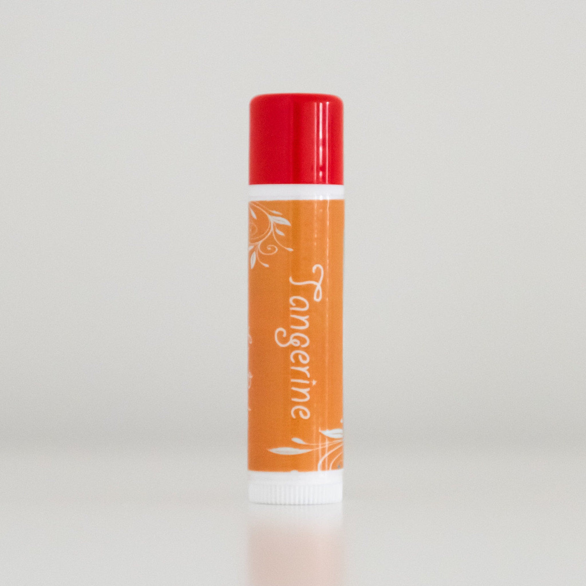 Tangerine lip balm, orange and red tube with white floral design, vertical presentation