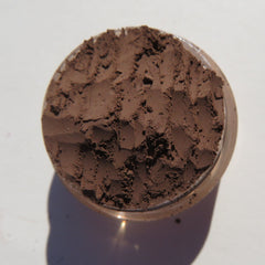 Side view of dark matte brown mineral eye shadow in open jar with loose powder texture and minimalist label