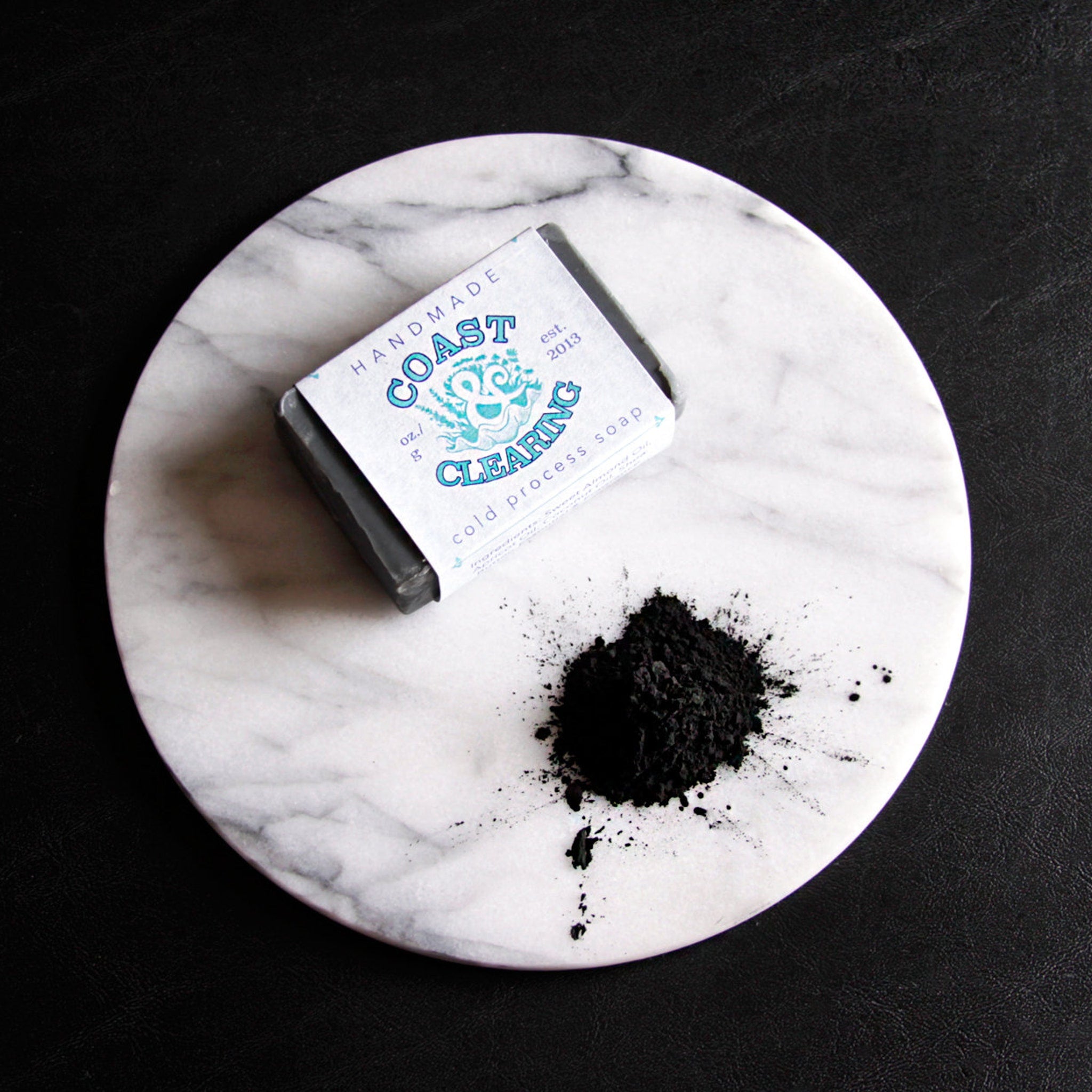 Facial cleanser bar, black soap on marble, Coast & Clearing brand visible