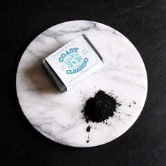 Facial cleanser bar, black soap on marble, Coast & Clearing brand visible