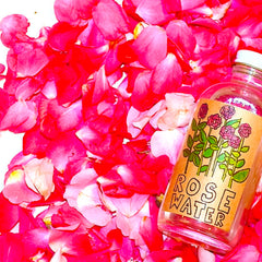 Rose water bottle with red rose petals, clear glass, and ROSE WATER label