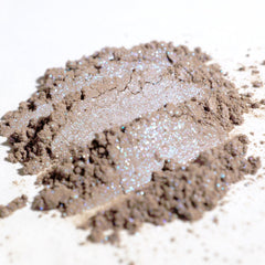 Hand applying taupe eyeshadow with silver and iridescent blue shimmer to eyelid using a brush