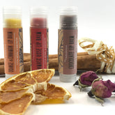 Lip balms with orange, red, and brown tubes, with myHerbalicious labels, and dried fruit and flowers