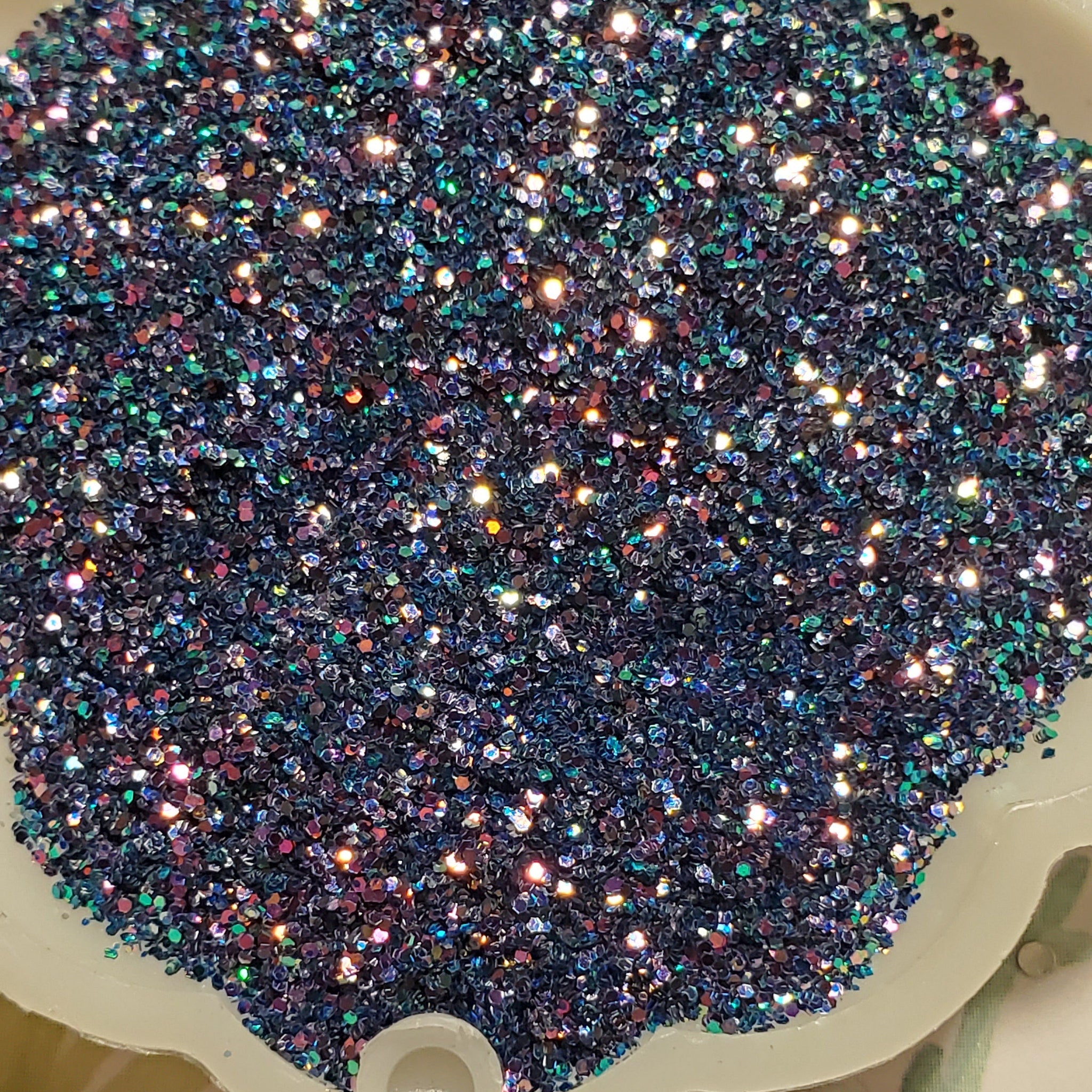 Glitter eye shadow in dark blue with iridescent sparkle, in a white dish