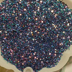 Glitter eye shadow in dark blue with iridescent sparkle, in a white dish