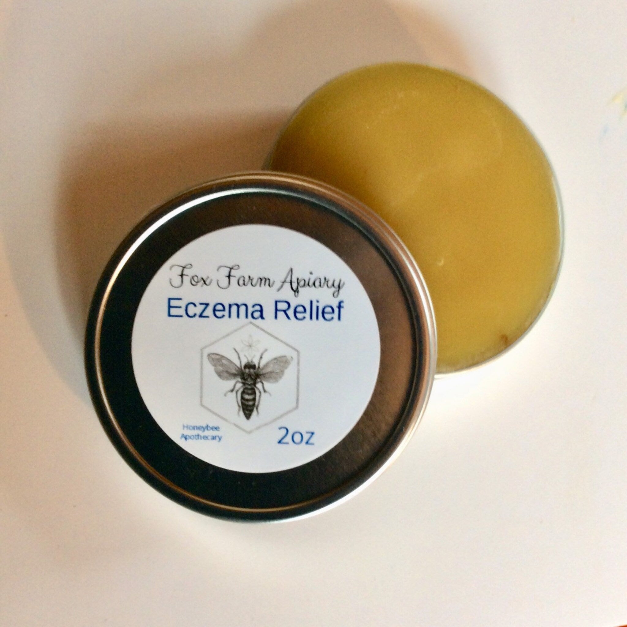 Skin care eczema relief product with yellow balm, metal tin, and Fox Farm Apiary label