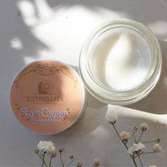 Eye cream jar with white cream and Estrellita Natural branding, open on table with flowers