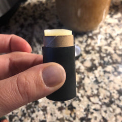 Lip balm tube with black sleeve, cardboard tube, and pale yellow balm held in hand