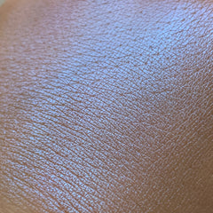 Close-up of fingertips applying shimmering blue eye shadow to eyelid with soft blending brush