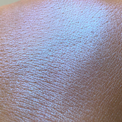 Close-up of vibrant blue eye shadow pigment with shimmering metallic finish in a small round pot