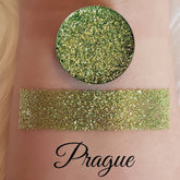 Glitter eyeshadow with green and gold glitter, swatched on skin, "Prague" text visible