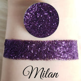 Glitter eyeshadow swatch with purple glitter, Milan brand visible, applied to skin