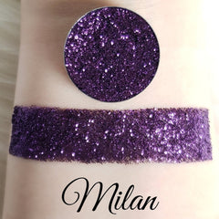 Glitter eyeshadow swatch with purple glitter, Milan brand visible, applied to skin
