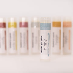 Lip balm tube with white, blue, and clear plastic, "bushel & a peck ginny" text visible