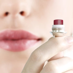 Lipstick tube with red lipstick, white and silver components, held by a hand near lips