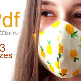 White cotton face mask with adjustable ear loops, lying flat to show layered fabric construction and stitching details